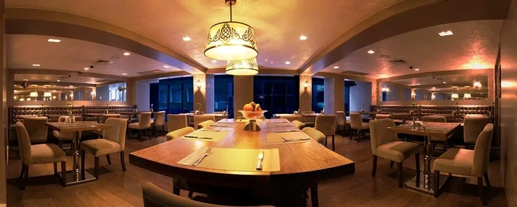 A wide angle photo of a warmly lit restaurant with minimalistic wood and metal aesthetic